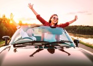 Happy younger couple standing in convertible car with arms up
